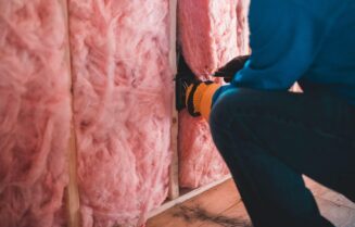 Crop unrecognizable worker in gloves sitting on haunches and insulating with pink stone wool